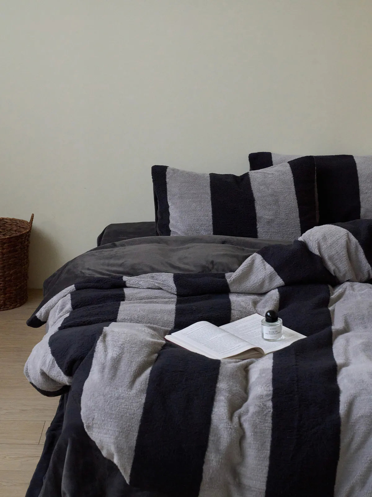 Full view of the plush black and grey striped fleece bedding set on a bed in a minimalist room with a book resting on top. - RoomDen