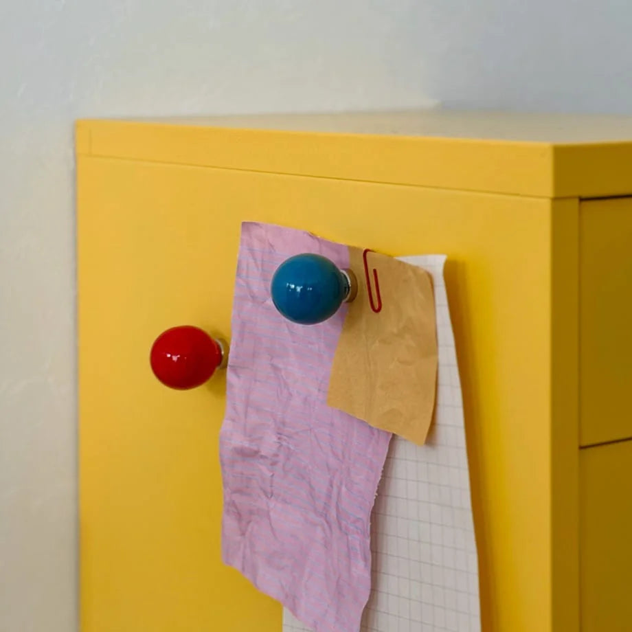 Red and blue magnetic hooks holding notes on a vibrant yellow metal cabinet. - RoomDen