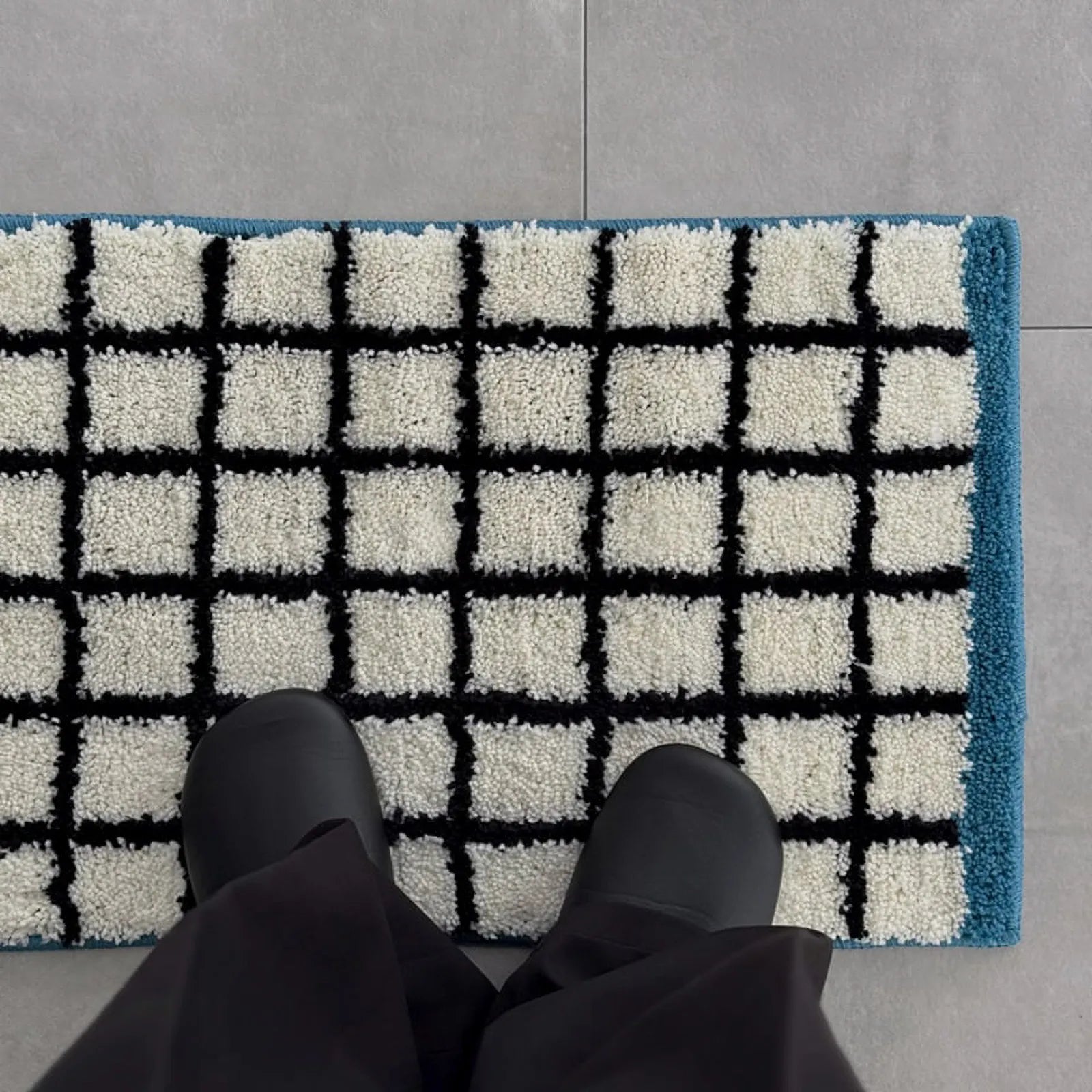 Top-down perspective of black shoes standing on the soft white and black grid rug - RoomDen