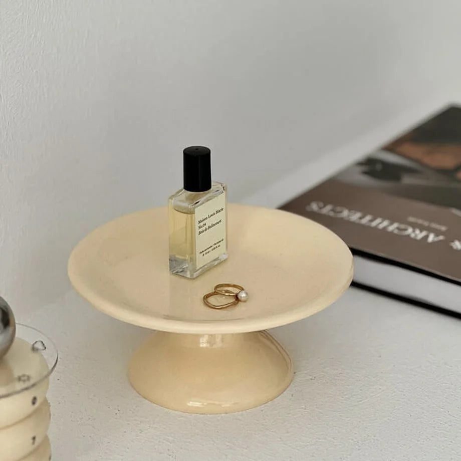 Top-down view of the creamy beige jewelry dish holding two gold rings with a pearl. - RoomDen