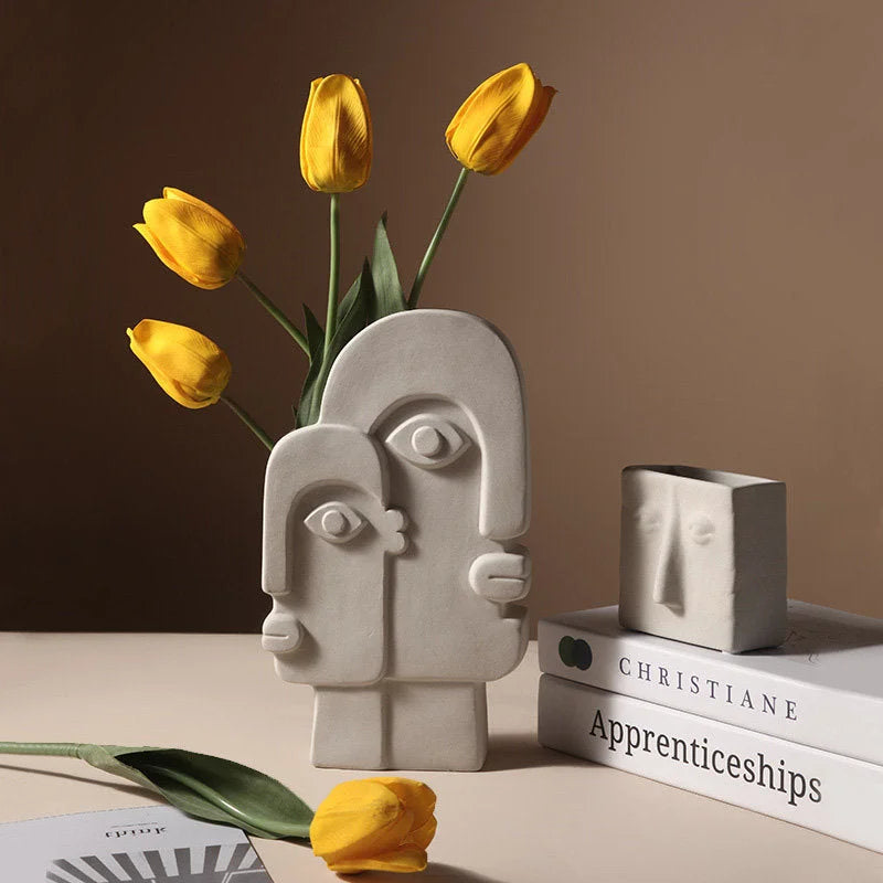 A collection of Wabi-Sabi inspired face vases in stone grey, one holding yellow tulips - RoomDen.