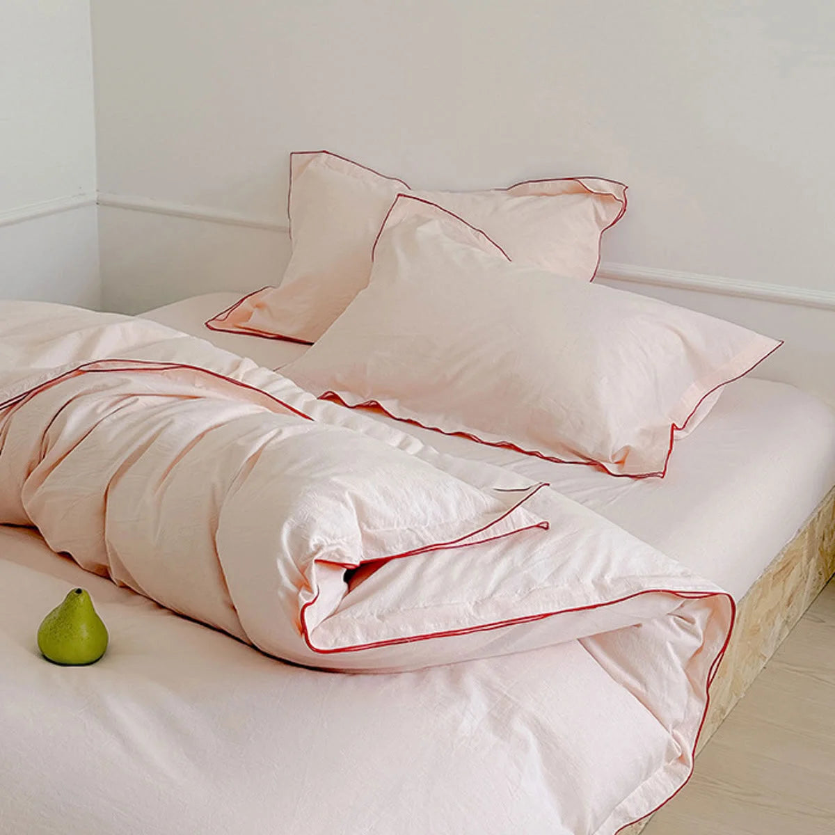 A bed with blush pink ruffle trim bedding set, styled on a simple wooden platform frame. - RoomDen