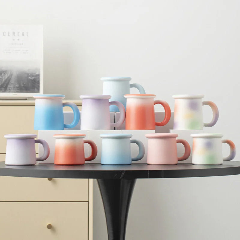 A collection of Frosted Ombre Ceramic Mugs in various pastel colors on a black table - RoomDen.