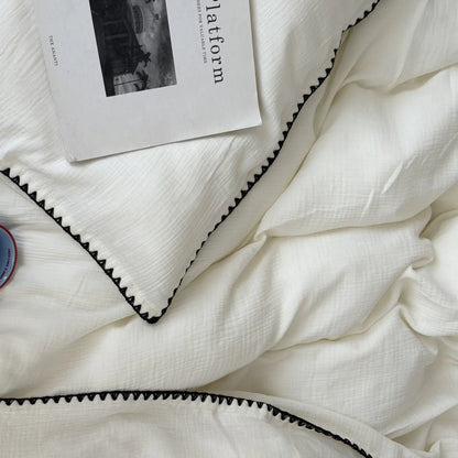 Detail of the black embroidered edge on the soft, crinkled cream white washed cotton duvet cover.