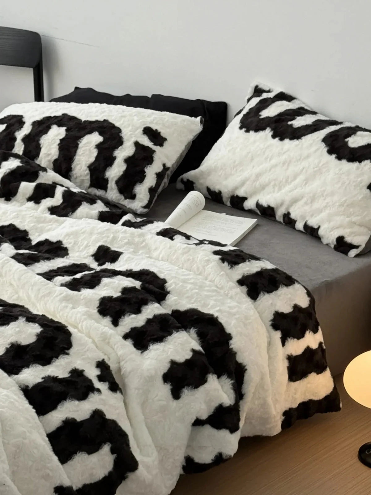 Lifestyle image of the plush text print bedding set, showing the duvet draped over the side of the bed next to a warm lamp. - RoomDen
