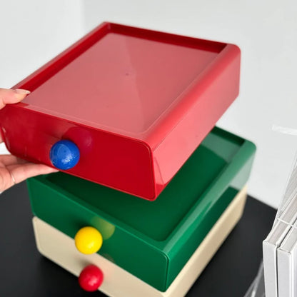 A hand lifting the red drawer from the stack, showing the modular design of the organizer. - RoomDen