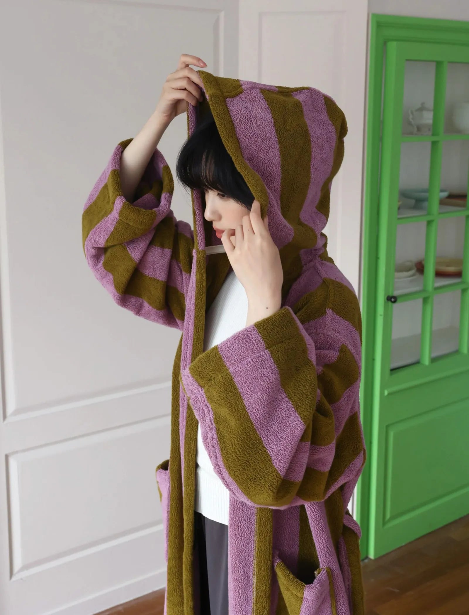 Woman putting on the hood of the purple and green striped bath gown.