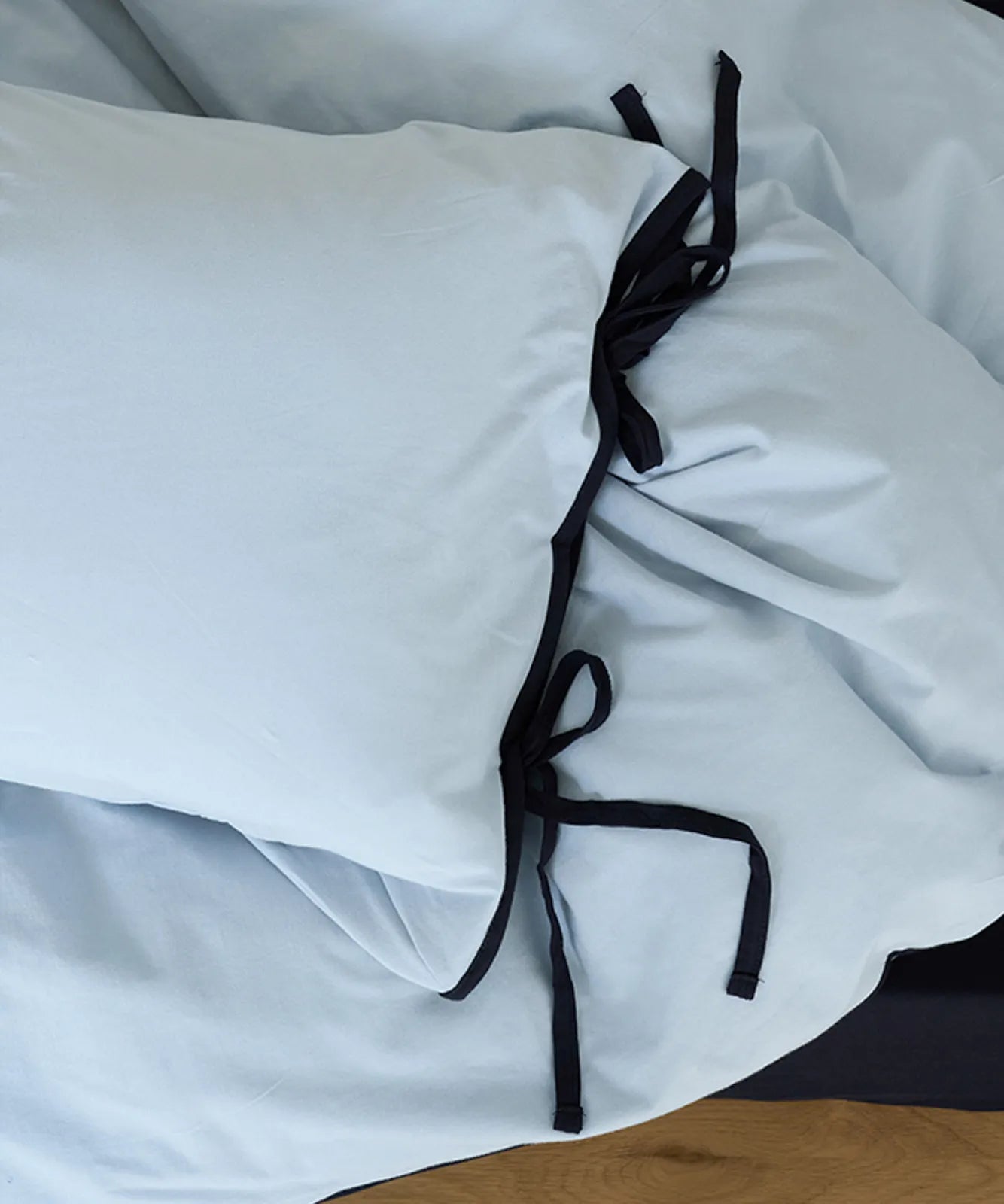 Close-up detail of the black tie on the corner of the sky blue pillowcase. - RoomDen