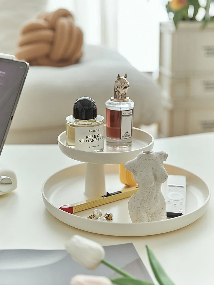 Cream white two-tier organizer tray on a coffee table with perfume bottles and a small sculpture. - RoomDen