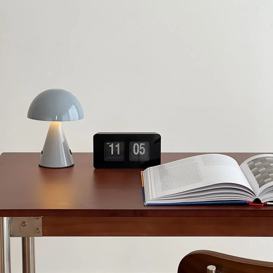 All-black retro flip clock on a dark wood desk with a book and a grey lamp, showing 11:05 AM. - RoomDen