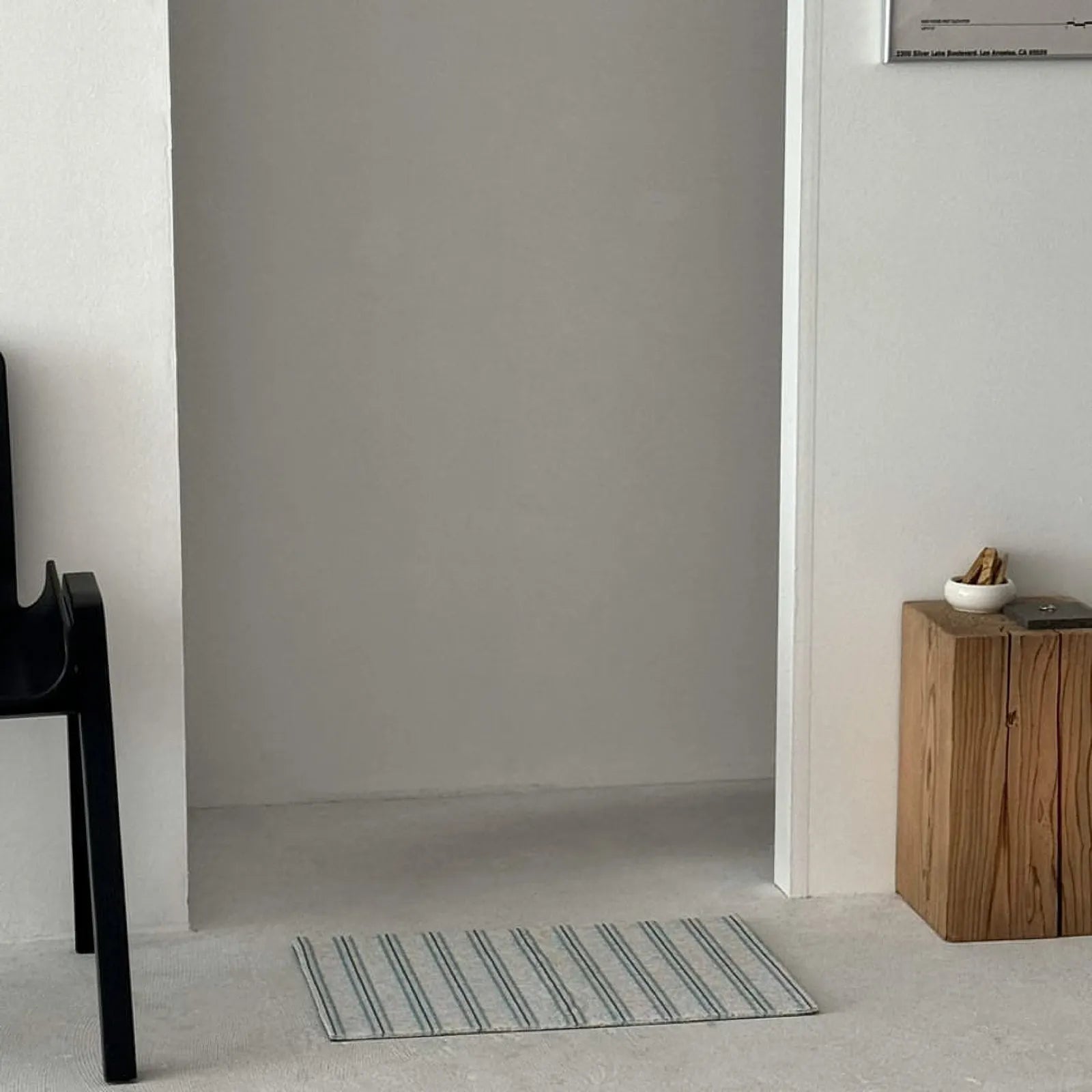 Blue and grey striped PVC coil rug placed in a minimalist white room doorway - RoomDen