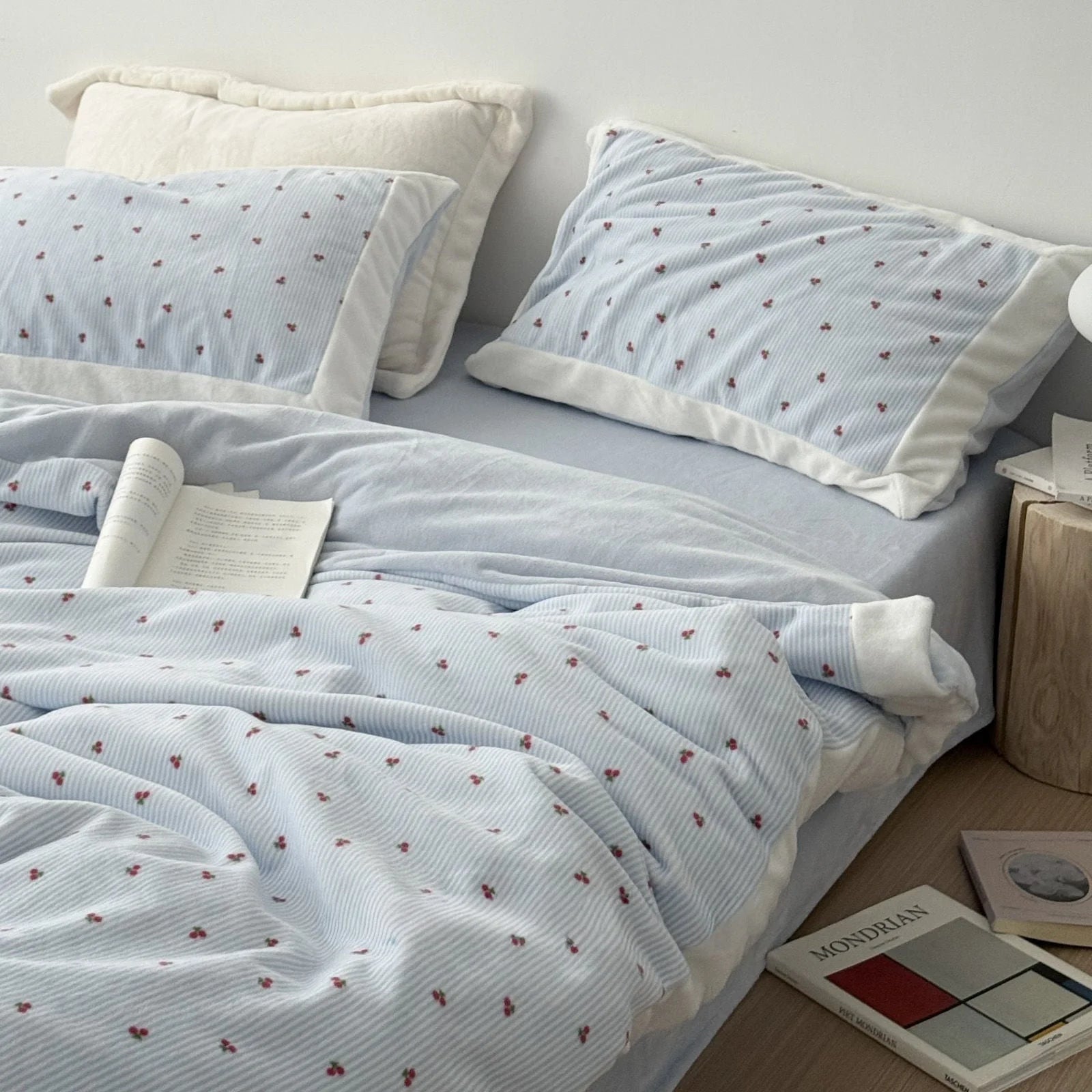 Lifestyle image of the cherry pinstripe flannel fleece bedding in a well-lit bedroom, with books on the floor suggesting a relaxing atmosphere - RoomDen.