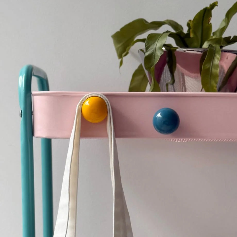Close-up of a Yellow magnetic hook holding a tote bag on a pink cart, with a blue hook nearby. - RoomDen