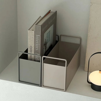 Two minimalist metal desktop organizers, one slate grey and one warm beige, holding books on a white shelf. - RoomDen