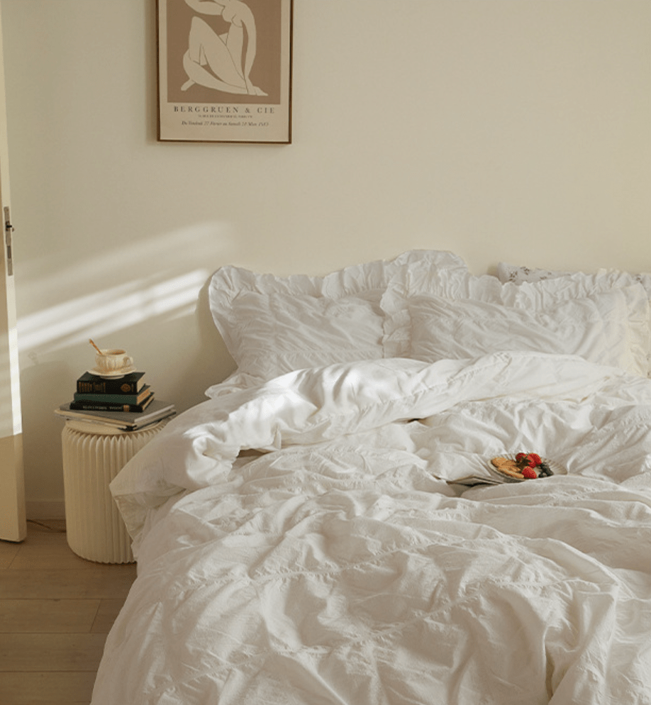 Odessa Ruffled Cotton Blend Bedding Set – ivory bedding viewed from the side beside books and framed artwork - Roomden