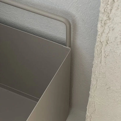 Close-up of the warm beige metal organizer's handle against a textured white wall, showcasing its Wabi-Sabi aesthetic.