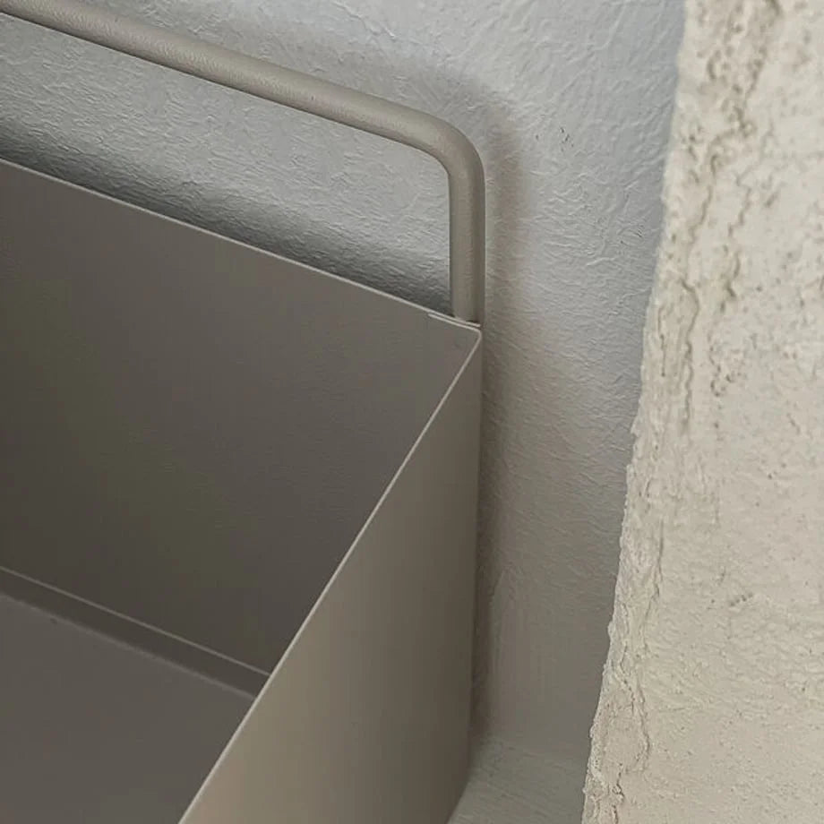 Close-up of the warm beige metal organizer's handle against a textured white wall, showcasing its Wabi-Sabi aesthetic.