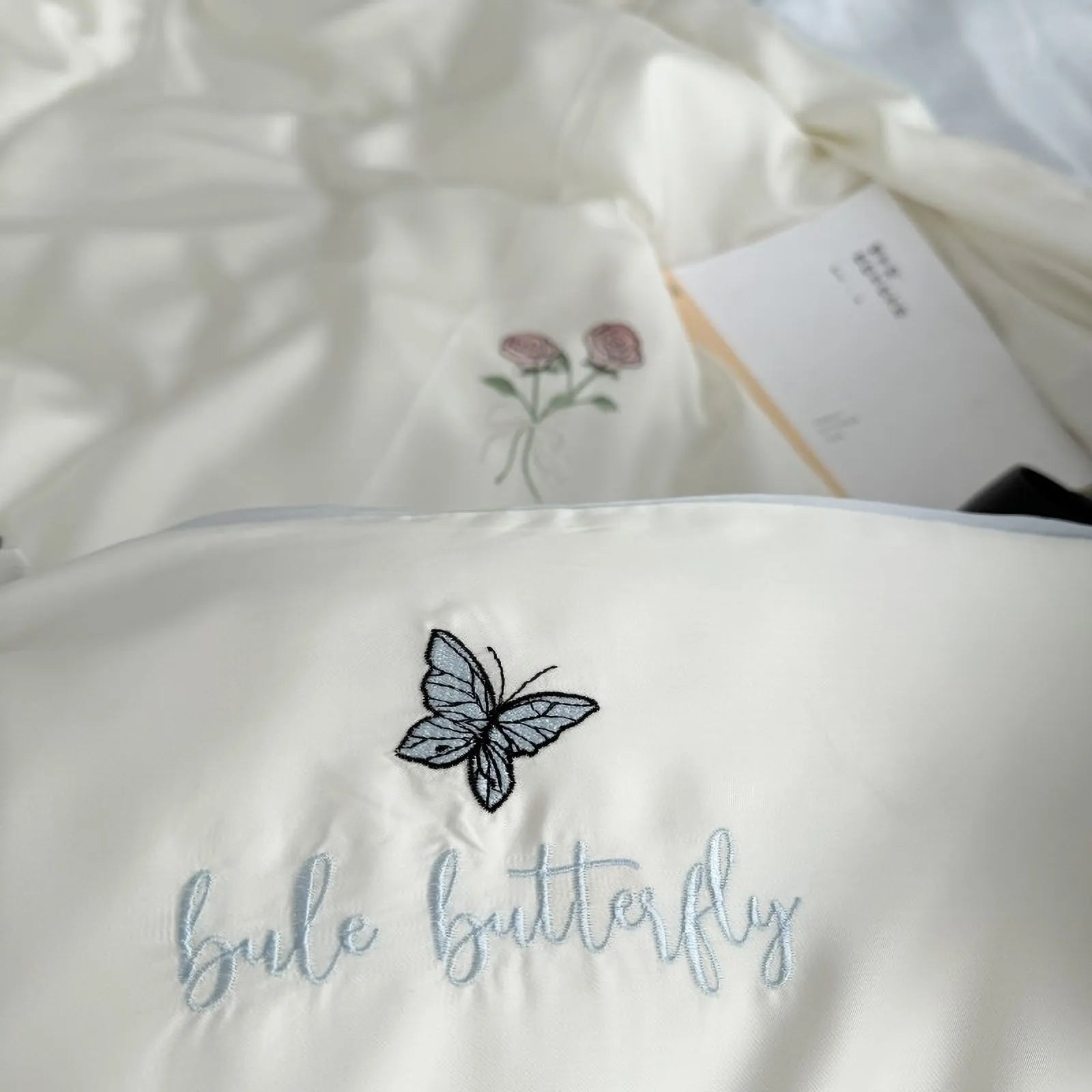 Detailed shot of the "blue butterfly" text embroidery on the Cream White pillowcase, made from silky Tencel fabric.