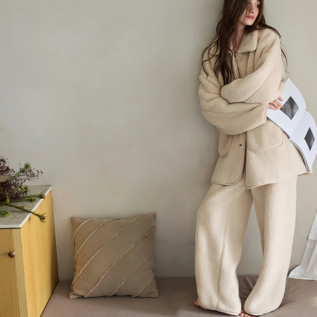 Model leaning against a wall and holding a magazine, wearing the Creamy Beige Fleece Pajama pants and jacket.
