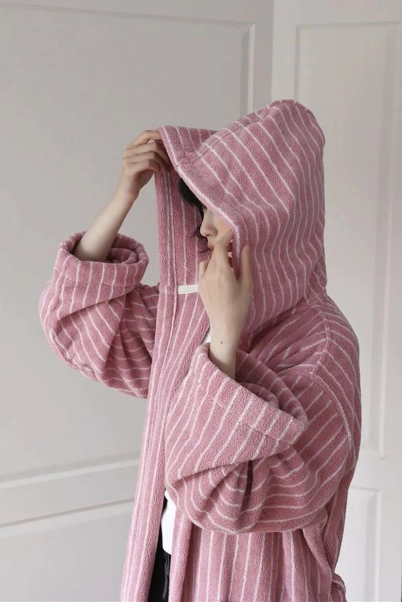 Woman pulling up the hood of the soft pink striped terry cloth robe - RoomDen