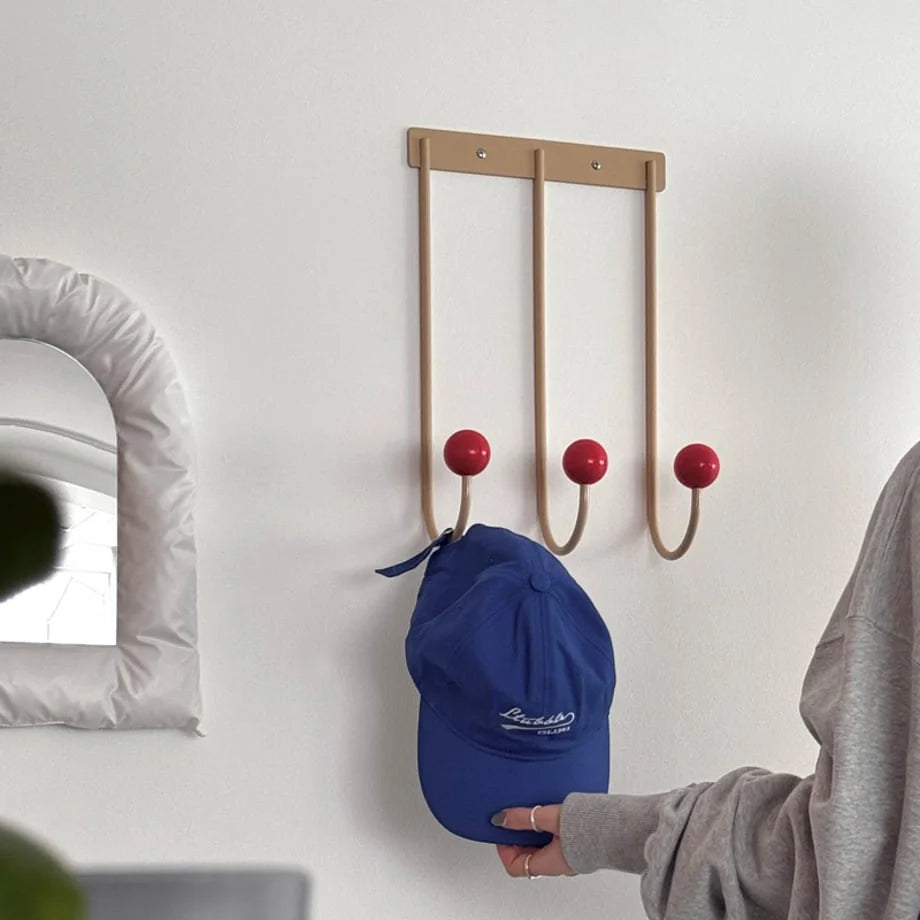 The Beige & Red Metal Wall Hooks holding a blue baseball cap in a room with a puffy white mirror. - RoomDen