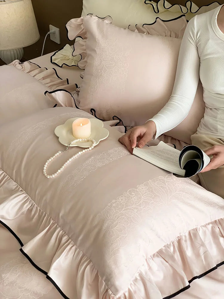 A person reading in bed on the Blush Pink ruffled bedding, showing a close-up of the jacquard stripe on the pillow - RoomDen.