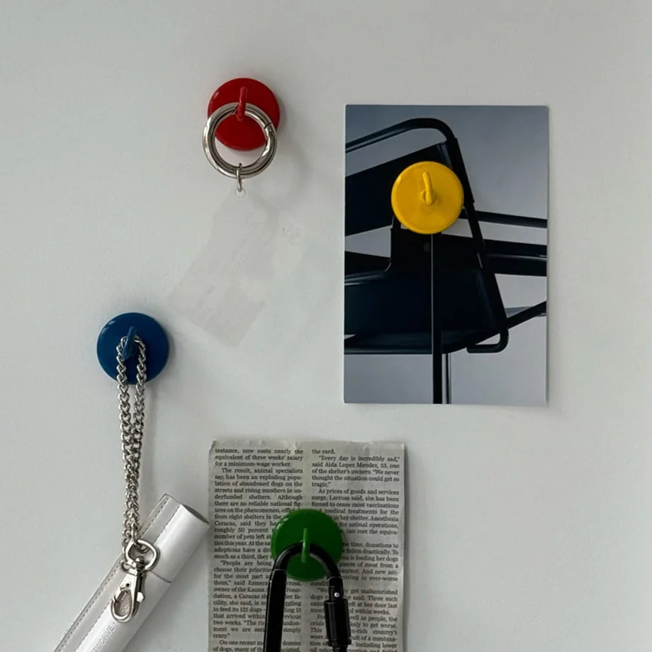 Top-down view of red, yellow, blue, and green magnetic metal hooks organizing items on a white refrigerator door - RoomDen