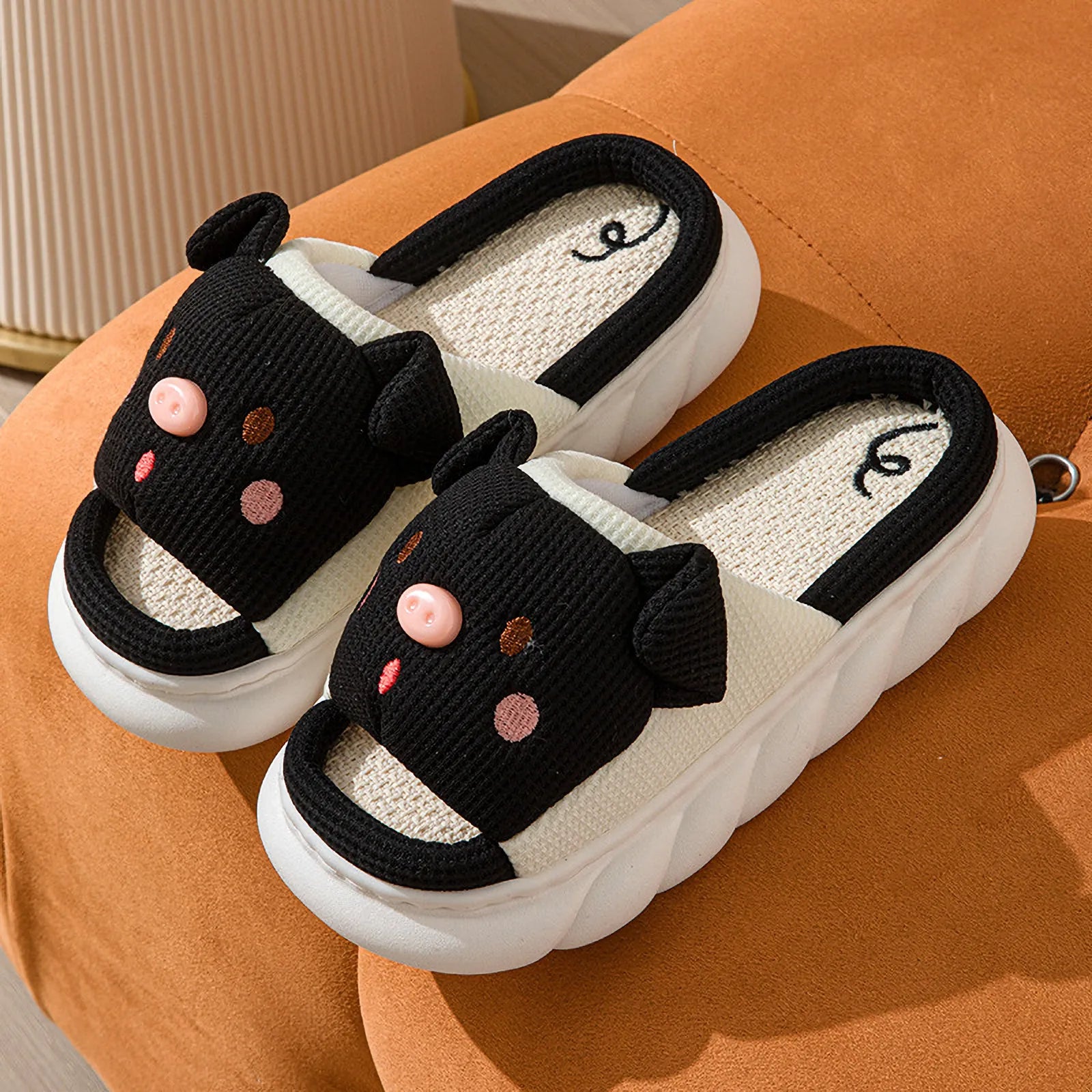 Pair of Black Waffle Textured Embroidered Pig Linen House Slippers on an orange surface - RoomDen