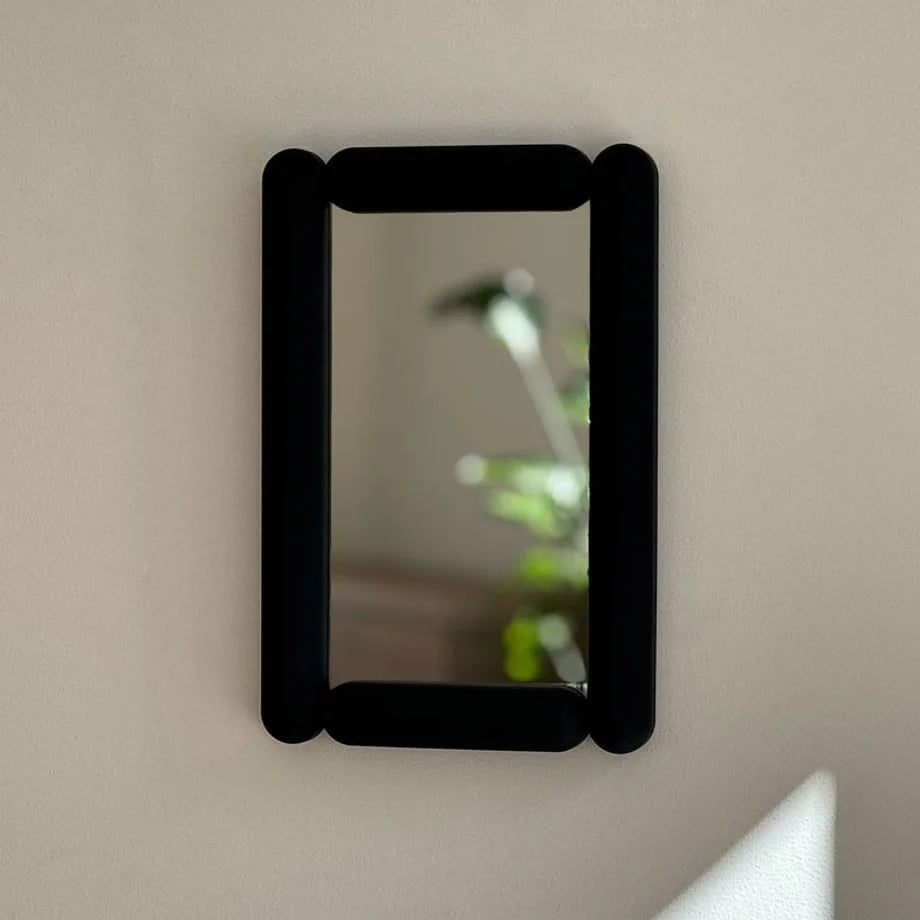 Black pill-shaped mirror mounted on a light-colored wall. - RoomDen