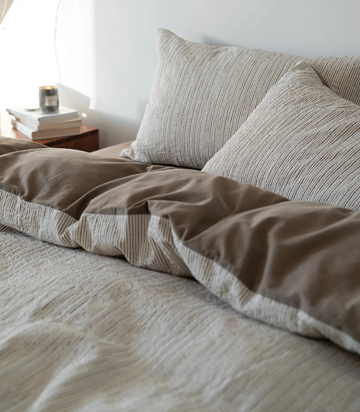 Side view of the Latte Brown pinstripe bedding showing the solid brown reverse side, with a candle on the nightstand.