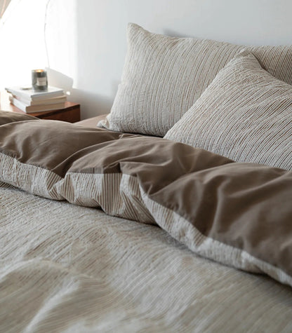 Side view of the Latte Brown pinstripe bedding showing the solid brown reverse side, with a candle on the nightstand.