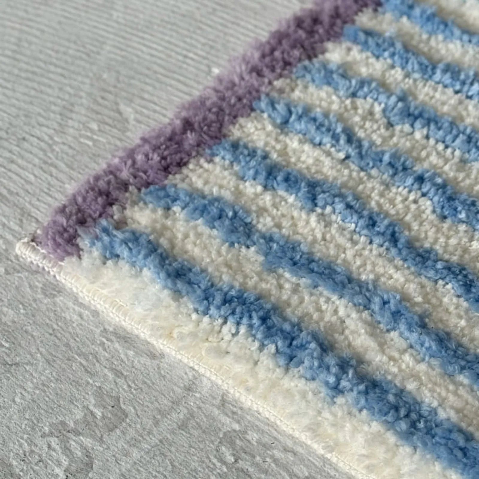 Close up of shaggy tufted texture and purple edge detail on striped rug