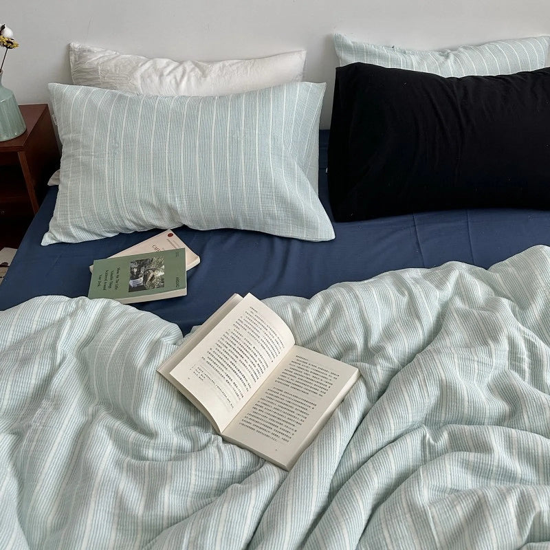 A bed styled with soft, textured washed cotton bedding, books, and a bedside table in a relaxed, airy room.