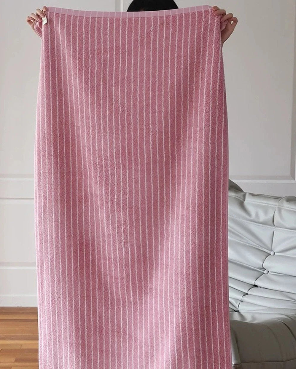 Full view of a pink and white pinstripe cotton bath towel held up to show its length and texture - RoomDen.