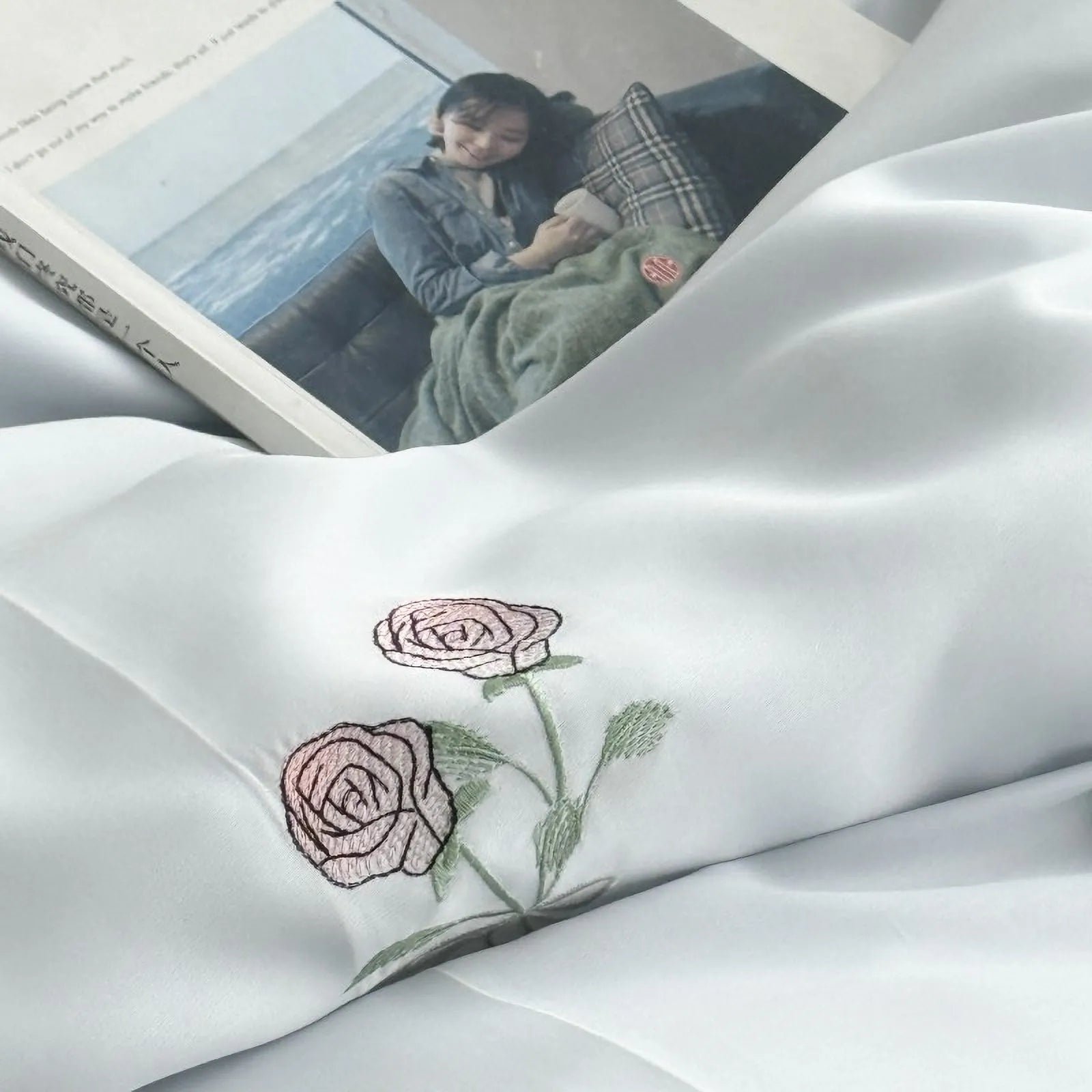 Close-up on the embroidered pink roses on the Cloud Blue duvet cover, with a book resting on the soft fabric.