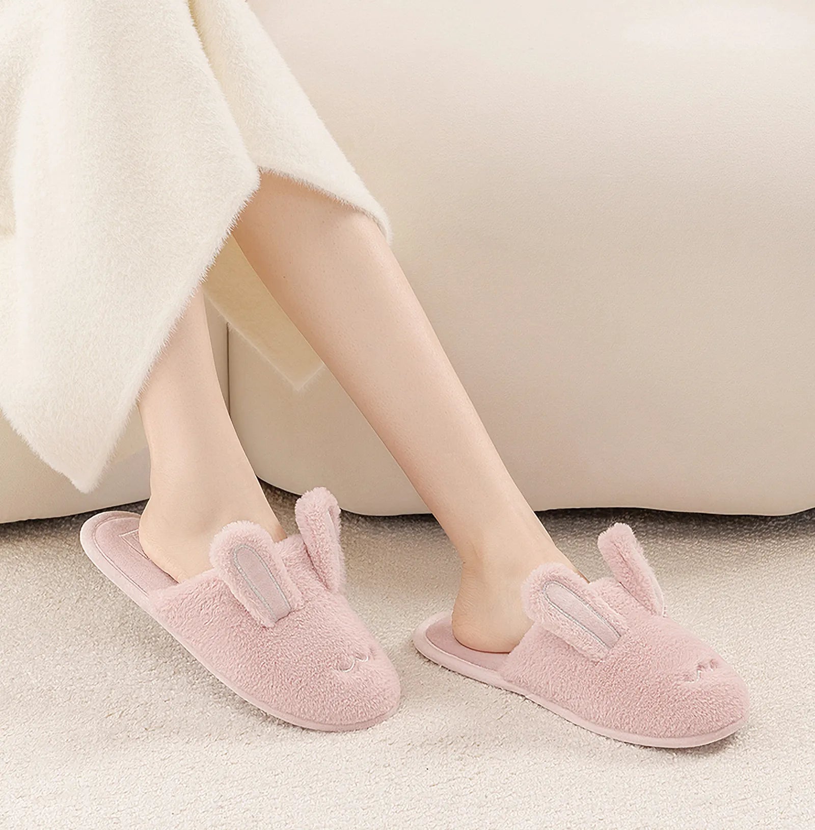 Pink plush bunny slippers on model legs sitting on white sofa - RoomDen
