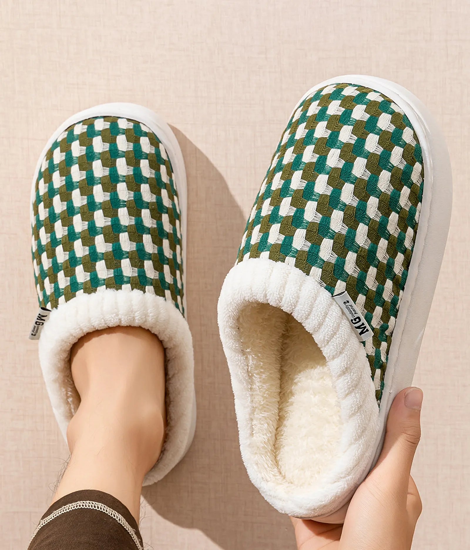 Top view of green woven gingham slippers held in hand showing plush interior - RoomDen