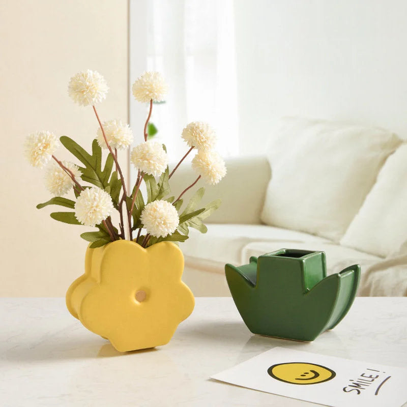 The Butter Yellow Daisy Bloom Ceramic Vase holding white flowers, with the Forest Green leaf base next to it. - RoomDen