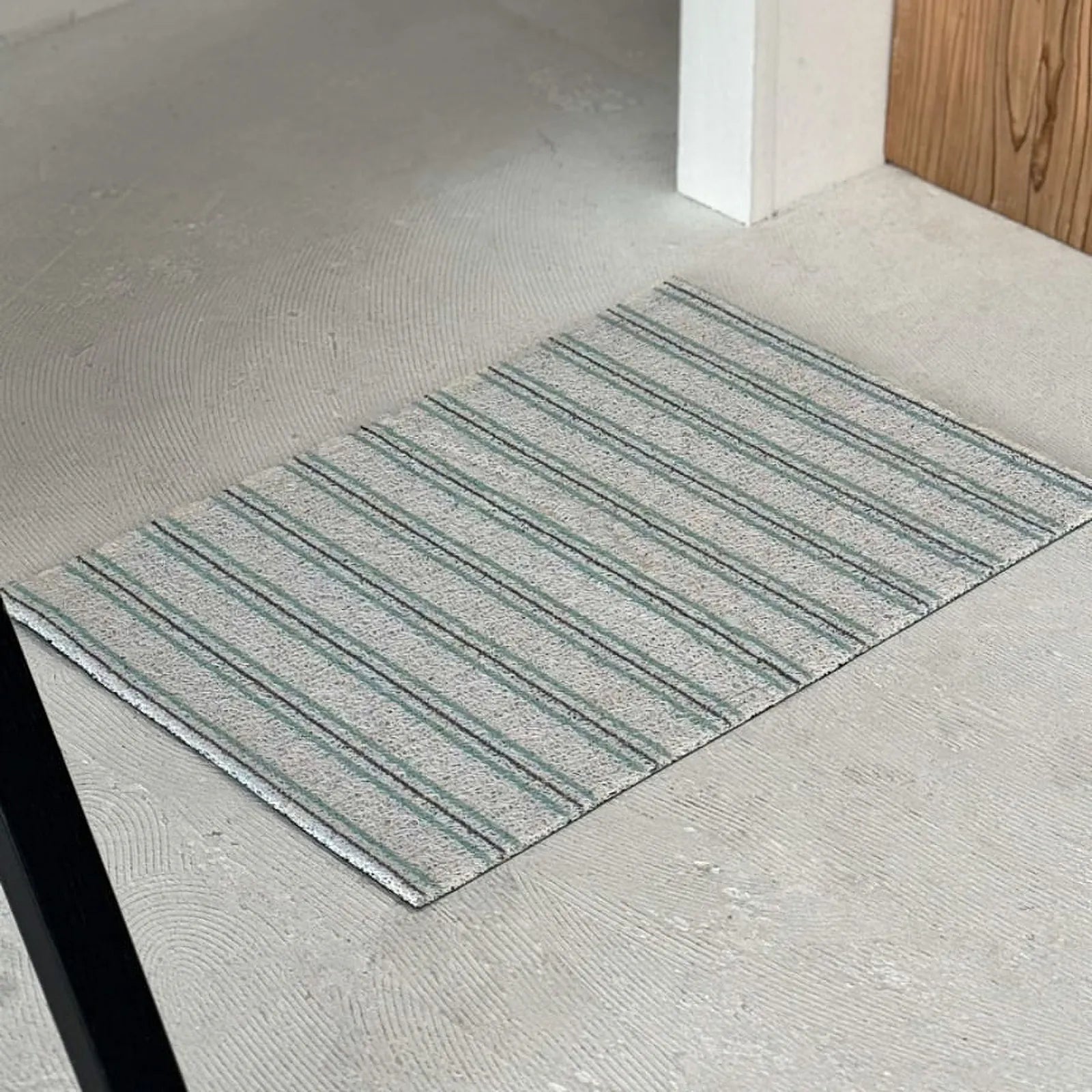 Blue and grey striped doormat on concrete floor near wooden furniture - RoomDen