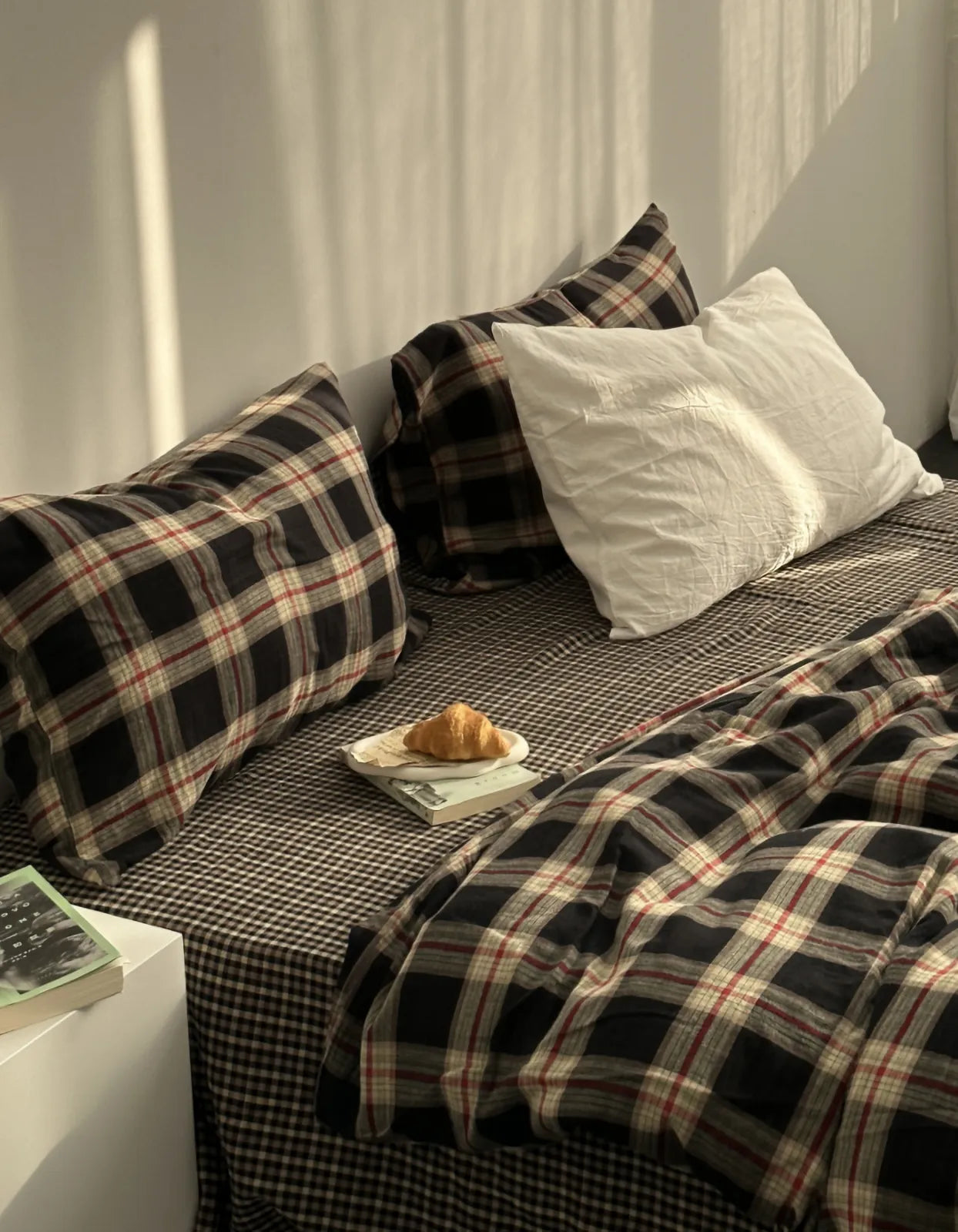 A cozy bed made with the Tartan Plaid & Gingham Washed Cotton Bedding Set, with a book and croissant nearby, evoking an autumn morning.