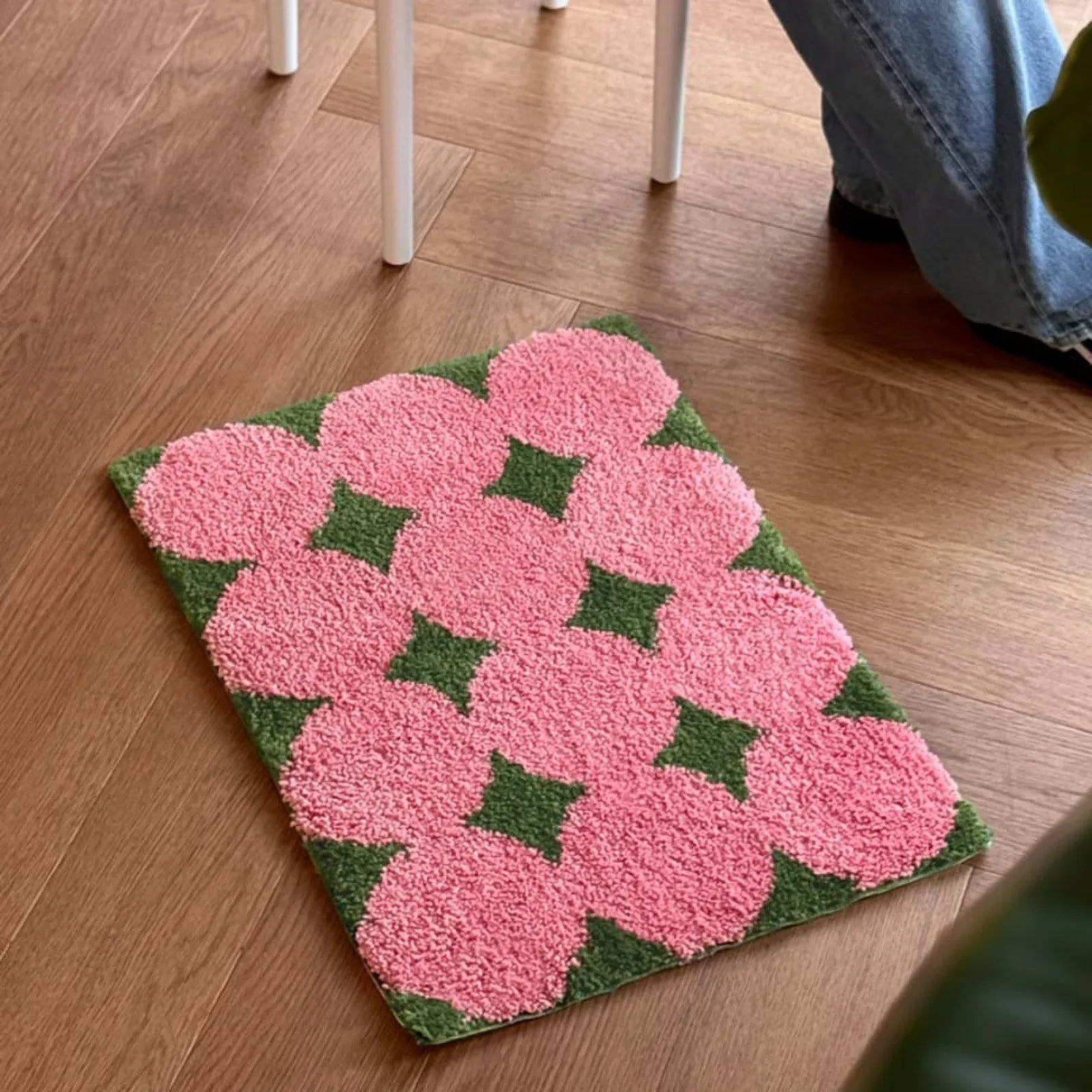 Person sitting on stool next to pink floral rug in living space - RoomDen