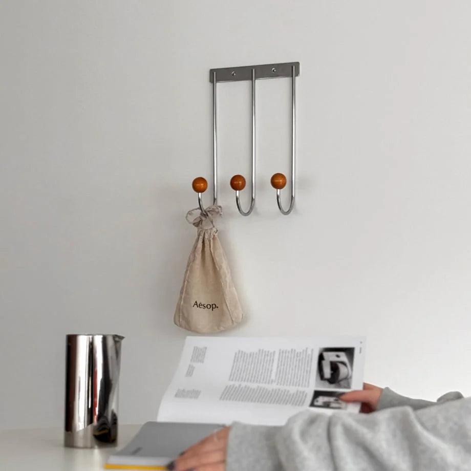 A person reading a magazine at a table with the Silver & Orange decorative hooks on the wall behind them. - RoomDen