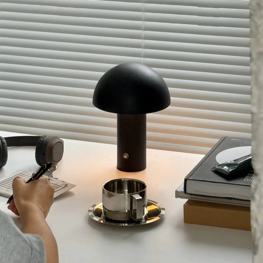 A person writing at a desk with the black Matte Minimalist Metal Mushroom Table Lamp providing warm light - RoomDen.