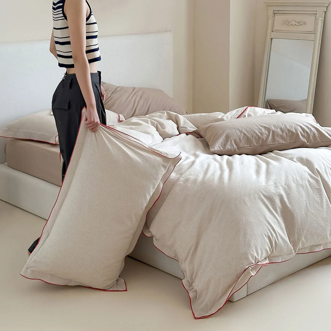 A woman holding a pillow from the Beige & Red Pinstripe Washed Cotton Bedding Set.