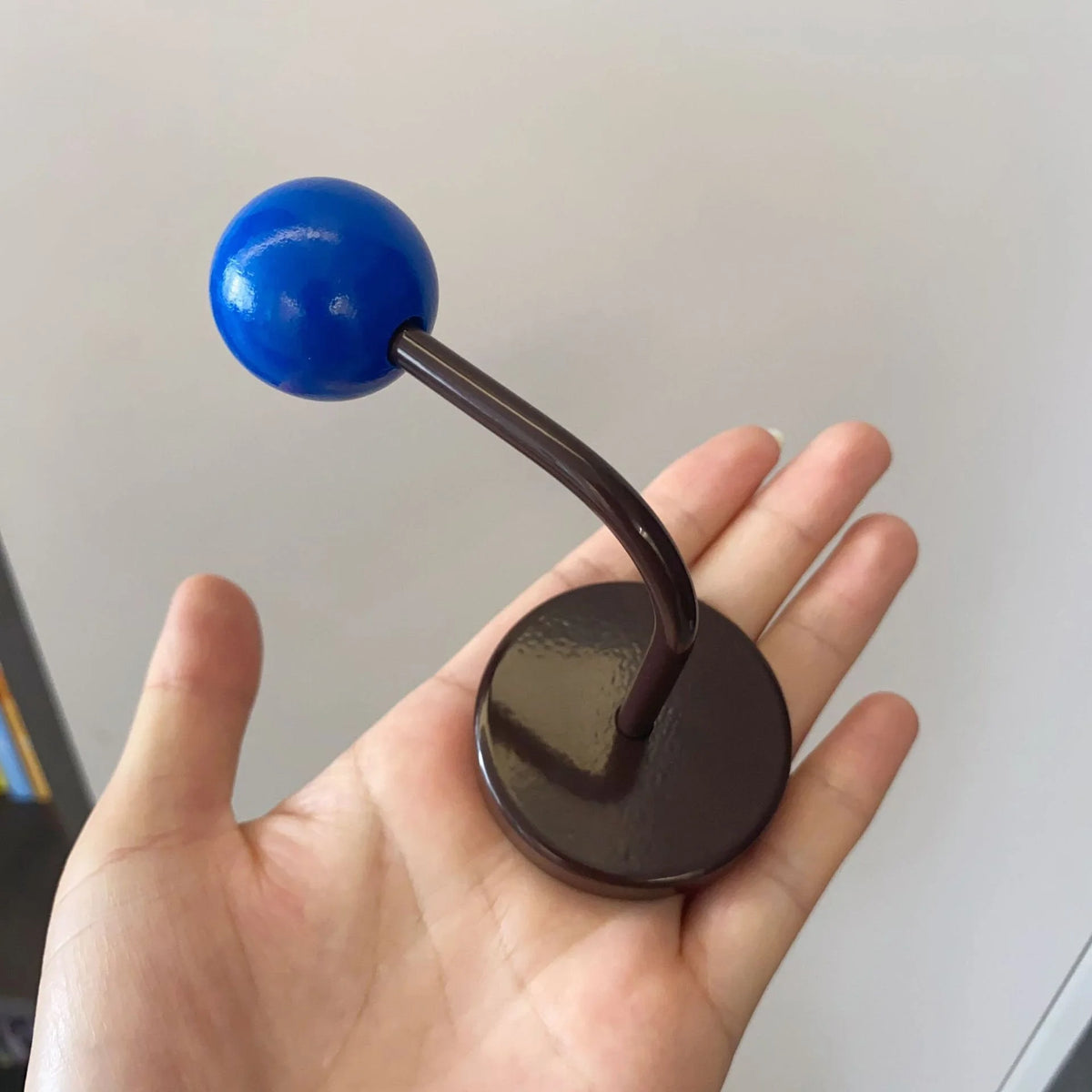 A hand holding the Blue & Brown Color Block Metal Hook to show its size and smooth finish - RoomDen.