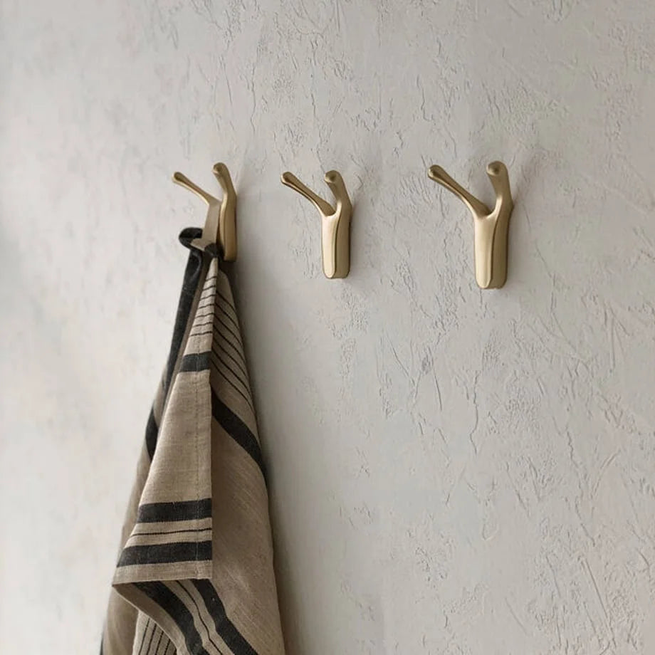 Angled view of the gold branch-shaped metal hooks on a wall, highlighting their matte finish - RoomDen