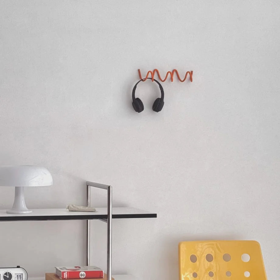 Headphones hanging on the orange Wavy Coil Metal Wall Hook above a modern shelf in a bright room. - RoomDen