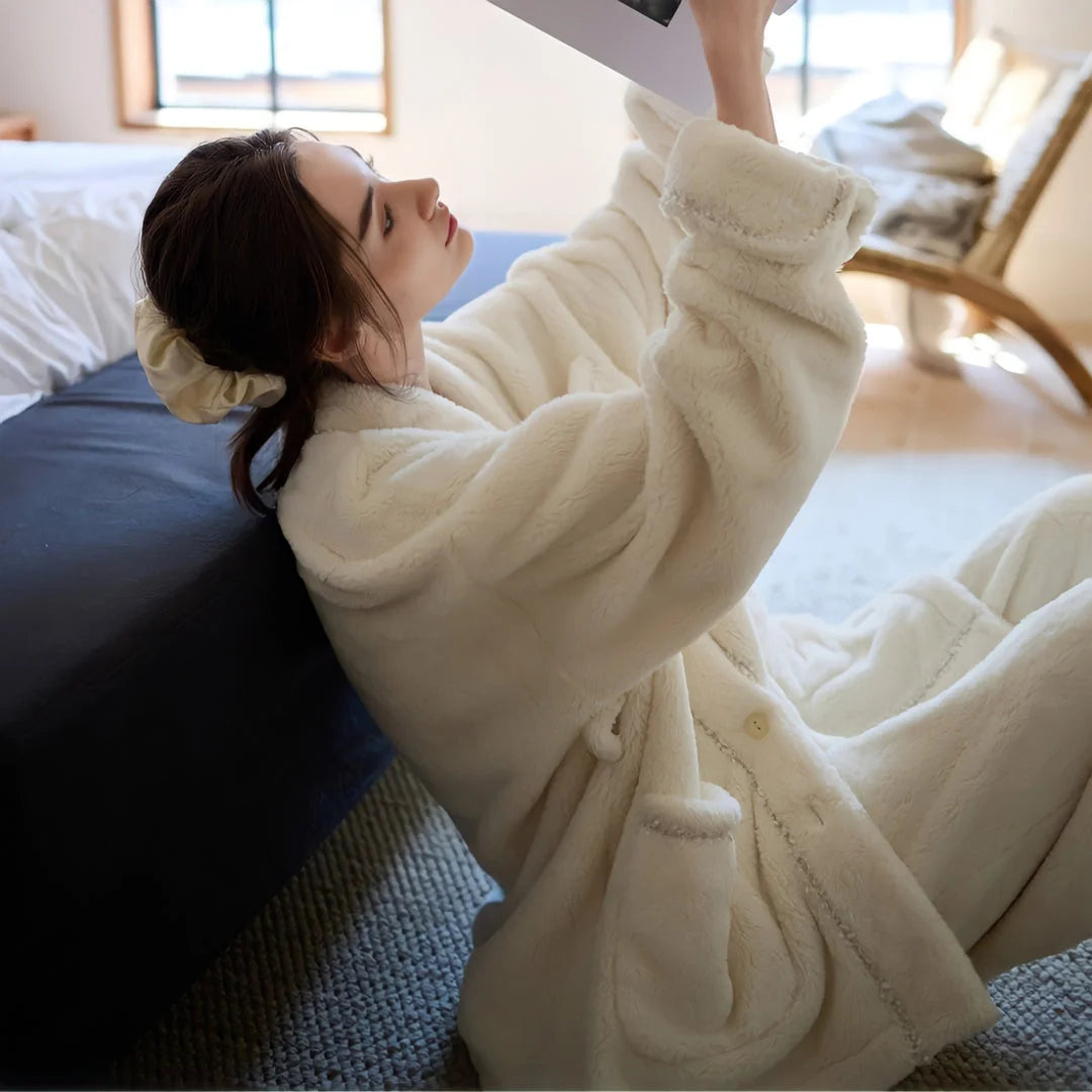 Model sitting on the floor, leaning against a bed and reading a book, wearing the relaxed-fit cream fleece pajama set - RoomDen.
