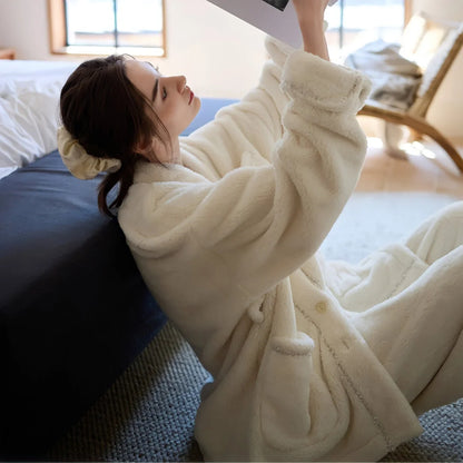 Model sitting on the floor, leaning against a bed and reading a book, wearing the relaxed-fit cream fleece pajama set - RoomDen.