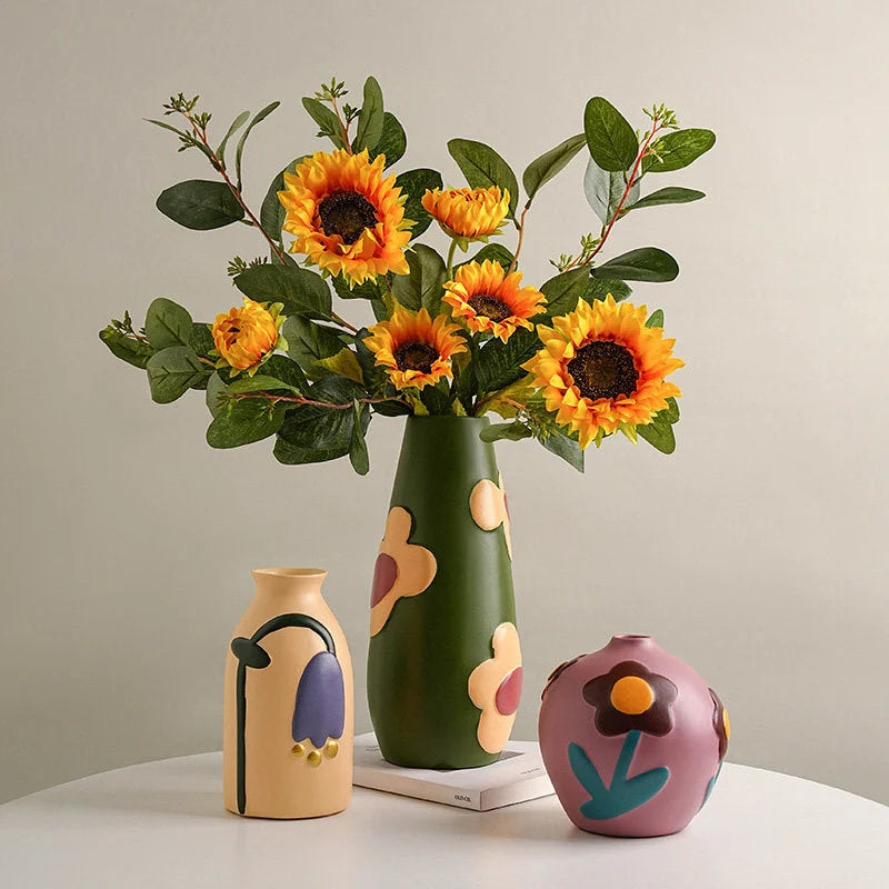 Three Pop Art Floral Ceramic Vases in green, beige, and mauve, displayed on a white table with sunflowers. - RoomDen